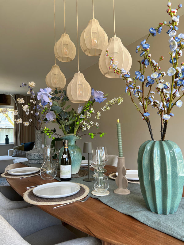 Gedekte houten eettafel met blauwe zijden bloemen in lage mintgroene vazen